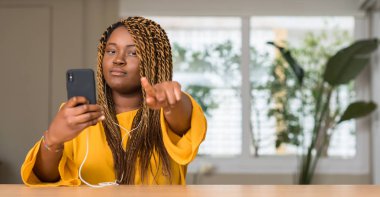 Parmak ile işaret kamera ve size, el işareti, pozitif ve kendinden emin bir jest ön kulaklık ile akıllı telefon kullanan Afrikalı-Amerikalı kadın