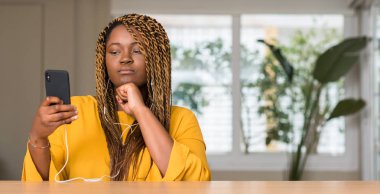 Afrikalı-Amerikalı kadın hakkında soru, çok düşünme kulaklık ciddi bir yüz ile Smartphone kullanarak fikir karışık