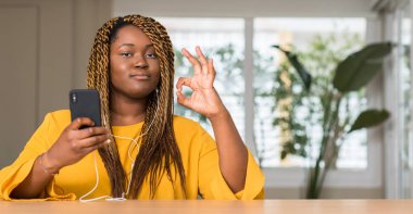 Afrikalı-Amerikalı kadın parmakları, mükemmel sembolü olan ok işareti yaptığını kulaklıklar ile Smartphone kullanarak