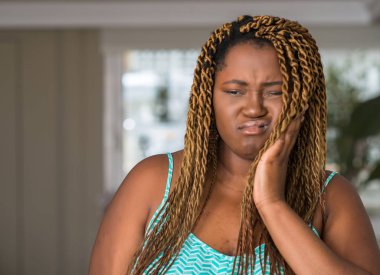 Afro-Amerikan kadına evde diş ağrısı veya dişlerde dişlerle ilgili hastalık nedeniyle ağız acı ifadesi ile el ile dokunmak. Diş hekimi kavramı.