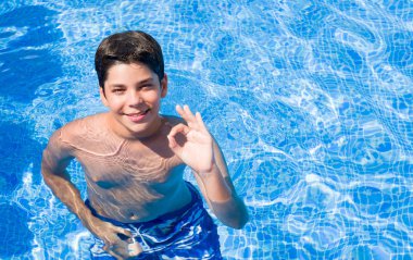 Tatil günlerinde genç çocuk parmak, mükemmel sembolü ile ok işareti yaparken plajda yüzme havuzunda