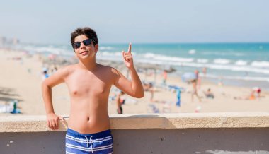 Plajda bir fikir ya da soru işaret parmağı ile gülen yüz, sürpriz tatil günlerinde genç çocuk bir numara