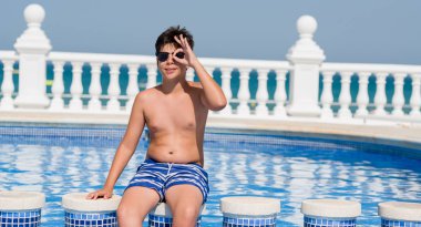 Mutlu yüz el parmaklarının arasından seyir göz üzerinde ok işaretiyle yapıyor gülümseyen ile plajda yüzme havuzunda genç çocuk tatilde