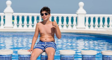 Genç çocuk tatilde plajda ok işareti, başparmak ile parmak, mükemmel işareti yapıyor kocaman bir gülümseme ile mutlu yüzme havuzunda