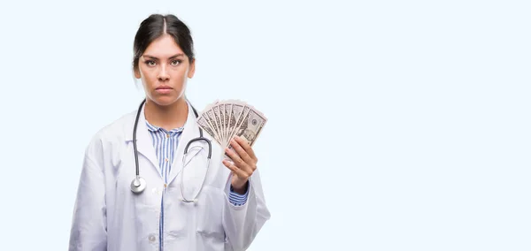 Jovem Hispânico Médico Mulher Segurando Dólares Com Uma Expressão Confiante — Fotografia de Stock