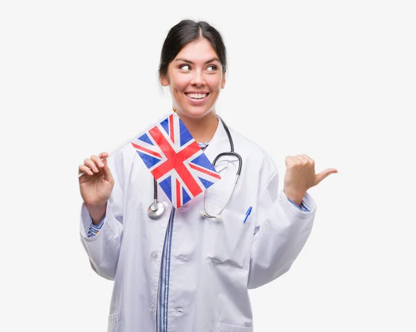 ヒスパニック系女医女性イギリスの旗を保持して指していると幸せそうな顔を笑顔で側まで親指で示す — ストック写真