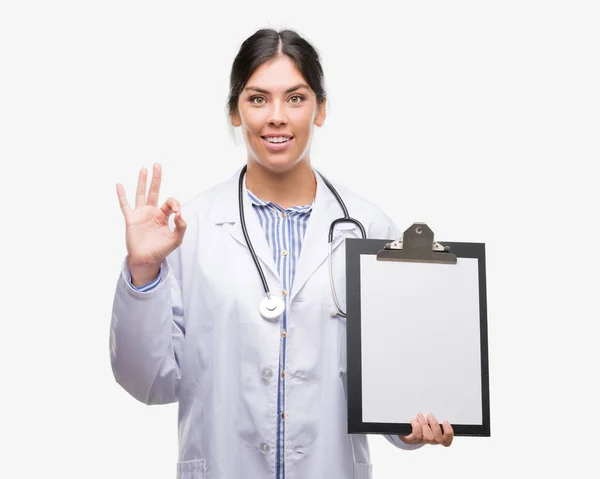 Jovem Hispânico Médico Mulher Segurando Prancheta Fazendo Sinal Com Dedos — Fotografia de Stock