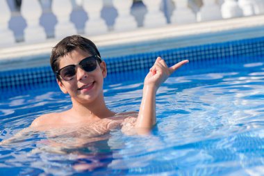 Genç çocuk tatilde plajda el ve parmak ile tarafına işaret çok mutlu yüzme havuzunda