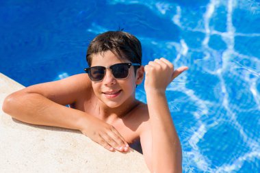 Genç çocuk tatilde plajda işaret ve başparmak kadar mutlu yüz gülümseyen tarafı ile gösterilen yüzme havuzunda