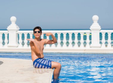 Genç çocuk tatilde plajda el ve parmak ile işaret çok mutlu yüzme havuzunda