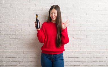 Genç Çinli kadın parmakları, mükemmel sembolü olan ok işareti yaparken bira içme tuğla duvarın üzerinden