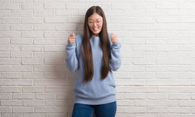 Zafer kutluyor gülümseyen genç Chinise kadın beyaz tuğla duvar silah ile başarı için heyecanlı kaldırdı. Kazanan kavramı.