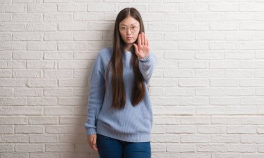 Genç Chinise kadın stop yapıyor beyaz tuğla duvar yüzünden elin avuç ile şarkı. Negatif ve ciddi bir jest yüz ifadesiyle uyarı.