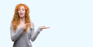 Hayret ve el ile sunulması ve parmak ile işaret ederken kameraya gülümseyen genç Kızıl saçlı kadın.