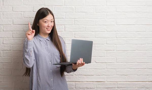 用笔记本电脑的年轻中国妇女用膝上型计算机惊讶的想法或问题指着一个快乐的脸 — 图库照片