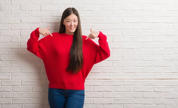 レンガ壁の顔に笑顔と自信を持って 誇りと幸せな指で自分を指している若い中国女性 — ストック写真