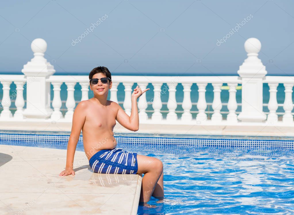 Young child on holiday at the swimming pool by the beach very happy pointing with hand and finger to the side