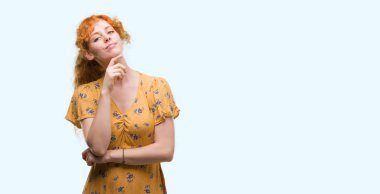 Çapraz kollar ve çeneme kaldırdı el ile gülümseme ile kameraya kendine güvenen arayan genç Kızıl saçlı kadın. Pozitif düşünce.