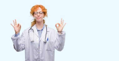 Genç Kızıl saçlı kadın giyen Doktor üniforma rahatla ve gülümseyen gözlerle kapalı parmak jestle meditasyon yapıyor. Yoga kavramı.