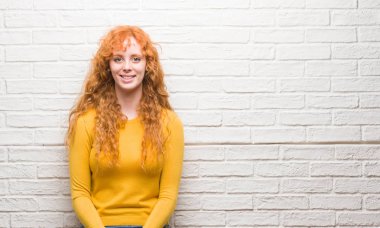 Bir gülen surat konumu olan tuğla duvar üzerinde duran ve diş gösterilen kendine güvenen bir gülümsemeyle gülümseyerek genç Kızıl saçlı kadın