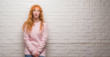Tuğla duvar korkuyor ve şok sürpriz ifade, korku ve heyecan yüz üzerinde duran genç Kızıl saçlı kadın.