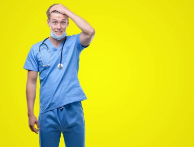 Genç yakışıklı sarışın doktor kafa üzerinde el ile vurguladı şok utanç ve sürpriz suratla, öfkeli ve sinirli. Korku ve hata için üzgün.