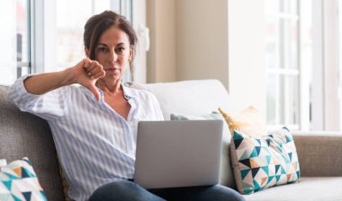 Orta yaşlı kadın kanepe kızgın yüzü, eksi işareti aşağı antipati başparmak ile gösterilen, ret kavramı ile dizüstü bilgisayar kullanarak