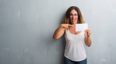 Boş kartı çok mutlu el ve parmak ile işaret tutan gri grunge duvarın üzerinden duran orta yaş İspanyol kadın