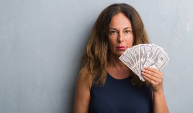 Dolar kendine güvenen bir ifade ile acımak yüz ciddi düşünüyorum tutarak gri grunge duvarın üzerinden duran orta yaş İspanyol kadın
