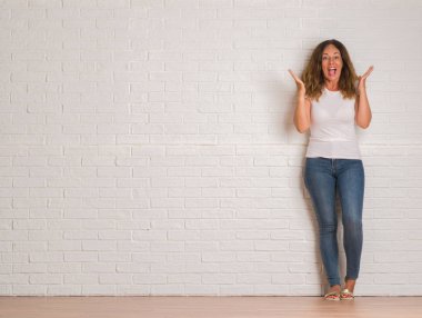 Kocaman bir gülümseme ile çığlık zaferini kutluyor beyaz tuğla duvar çok mutlu ve heyecanlı, kazanan ifade üzerinde duran ve ellerini kaldırdı orta yaş İspanyol kadın