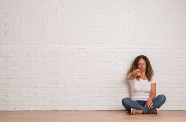 Orta yaş İspanyol kadın kamera ve size parmak ile işaret beyaz tuğla duvarın üzerinden, el işareti, pozitif ve kendinden emin bir jest ön