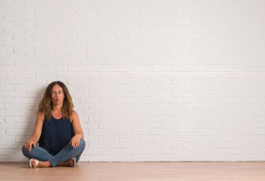 Orta yaş İspanyol kadın beyaz tuğla duvar yapım balık yüzüne dudaklı, çılgın ve komik bir jest yere oturma. Komik ifade.