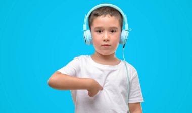 Koyu saçlı küçük çocuk müzik dinleme sürpriz ile kulaklık ile yüz kendine işaret parmağı