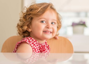 Oturan ve evde gülümseyen mavi gözlü güzel sarışın çocuğun.