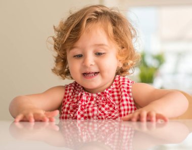 Oturan ve evde gülümseyen mavi gözlü güzel sarışın çocuğun.