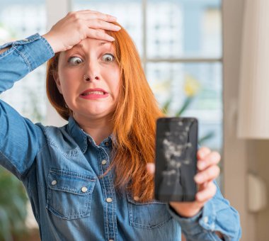 Kırık smartphone kafa üzerinde el ile vurguladı tutan Kızıl saçlı kadın şok utanç ve sürpriz suratla, öfkeli ve sinirli. Korku ve hata için üzgün.