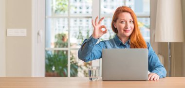 Kızıl saçlı kadının evde bilgisayar dizüstü kullanarak parmak, mükemmel sembolü ile ok işareti işi