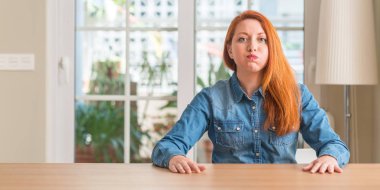 Kızıl saçlı kadın evde komik surat ile yanakları şişirme. Ağız ile hava, deli ifade şişirilmiş.