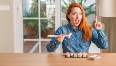 Kızıl saçlı kadın Chopsticks sürpriz bir fikir ya da soru işaret parmağı ile gülen yüz, bir numara kullanarak suşi yemek