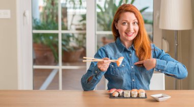Sürpriz yüz işaret parmağı kendine yemek çubukları kullanarak suşi yemek Kızıl saçlı kadın