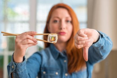 Yemek çubukları kullanarak kızgın yüzü, eksi işareti aşağı antipati başparmak ile gösterilen, ret kavramı ile suşi yemek Kızıl saçlı kadın