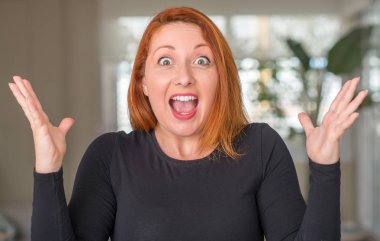 Kızıl saçlı kadın evde çok mutlu ve heyecanlı, kocaman bir gülümseme ile çığlık ve ellerini kaldırdı zaferini kutluyor kazanan ifade