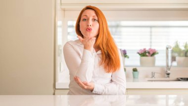 Bir öpücük el ile güzel ve seksi olmak hava üfleme kamera bakarak mutfak Kızıl saçlı kadın. Aşk ifade.