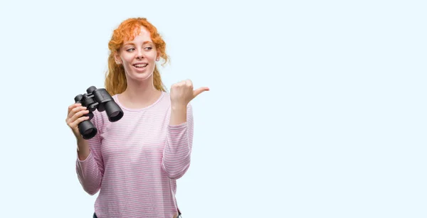 Young Redhead Woman Looking Binoculars Pointing Showing Thumb Side Happy — Stock Photo, Image