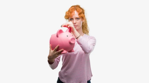 Junge Rothaarige Frau Hält Sparschwein Mit Selbstbewusstem Gesichtsausdruck — Stockfoto