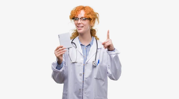 Young Redhead Doctor Woman Holding Blank Notebook Surprised Idea Question — Stock Photo, Image