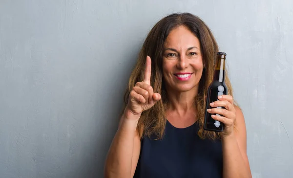 Midden Leeftijd Latino Vrouw Grijs Grunge Muur Holding Bierfles Verrast — Stockfoto