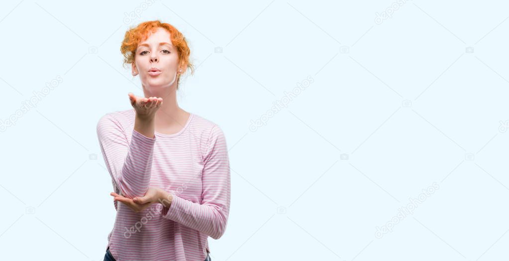 Young redhead woman looking at the camera blowing a kiss with hand on air being lovely and sexy. Love expression.