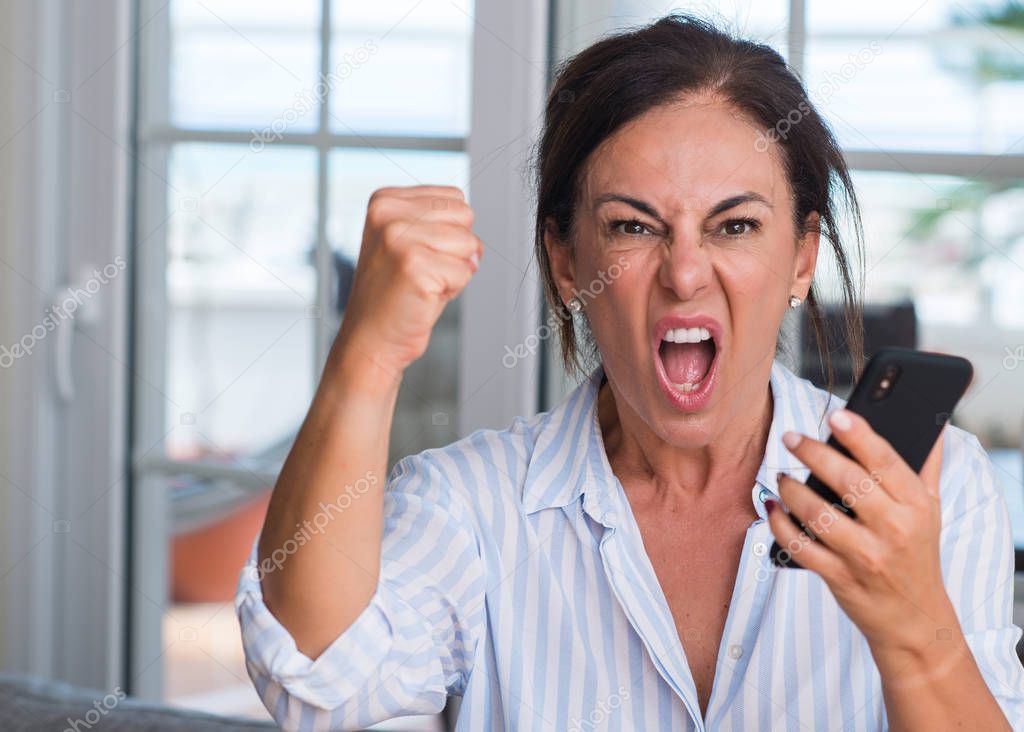 Middle aged woman using smartphone annoyed and frustrated shouting with anger, crazy and yelling with raised hand, anger concept
