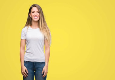 Ayakta ve diş gösterilen kendine güvenen bir gülümsemeyle gülümseyerek mutlu bir yüz ile t-shirt ve jeans giymiş güzel genç kadın